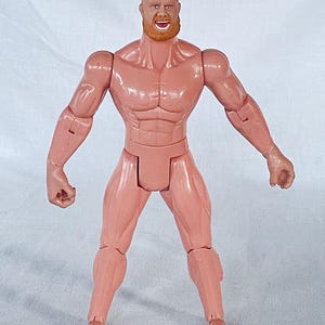 Pode incluir: Figura de ação rosa de um homem musculoso com cabeça careca e barba ruiva. A figura é articulada nas articulações e tem um físico detalhado, com definição muscular visível. A figura está em pé com os braços estendidos.