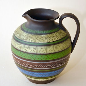 May include: A brown ceramic pitcher with a geometric pattern in green, yellow, blue, and brown. The pitcher has a wide base and a narrow neck.
