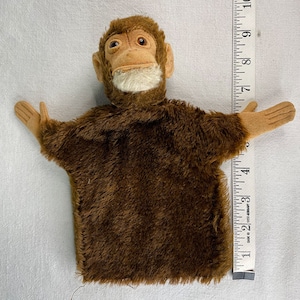 May include: Brown plush monkey puppet with a white face and brown eyes. The puppet is about 10 inches tall.