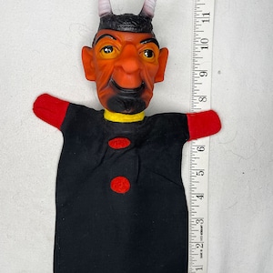 May include: A black puppet with a red and yellow collar, red sleeves, and two red buttons. The puppet has a brown face with a black beard, white horns, and a surprised expression. The puppet is 12 inches tall.