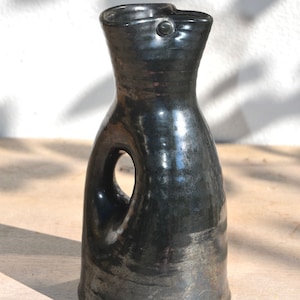 May include: A black ceramic pitcher with a unique handle design. The pitcher has a glossy finish and a slightly irregular shape.