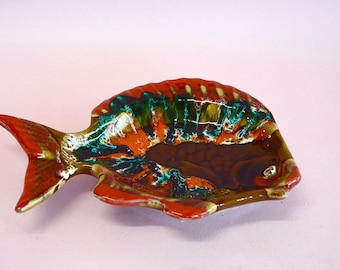 May include: A ceramic fish-shaped dish with a colorful glaze. The glaze features shades of brown, orange, green, and white. The dish is perfect for serving snacks or holding small items.
