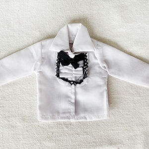 以下が含まれることがあります： 黒い蝶ネクタイとレースのトリムが付いた白い長袖シャツ