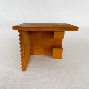 Può includere: Un piccolo modello di legno di un edificio con tetto e una parete laterale. L'edificio è fatto di legno marrone chiaro e ha un design semplice.