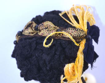 Puede incluir: Un sombrero de terciopelo negro con ribete estampado en dorado y marrón y un adorno de pluma amarilla.