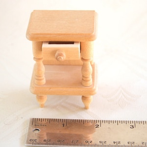 May include: A miniature wooden nightstand with a single drawer and turned legs. The nightstand is approximately 1 inch tall.