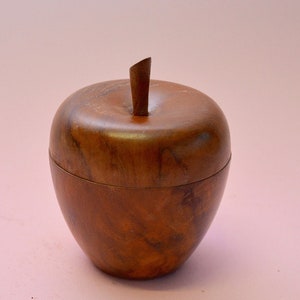 Puede incluir: Una caja de madera con forma de manzana con tapa. La caja está hecha de madera marrón oscura con un patrón de veta natural.