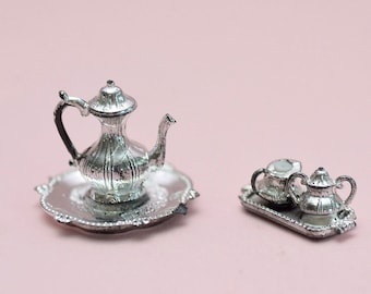 May include: A silver tea set with a teapot, creamer, and sugar bowl on a silver tray. The set is miniature in size and appears to be made of metal.