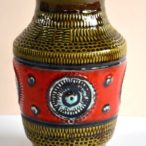 Puede incluir: Un jarrón de cerámica marrón y rojo con un patrón geométrico y una banda roja con círculos blancos y azules.