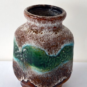Puede incluir: Un jarrón de cerámica marrón y blanco con un esmalte verde y azul. El jarrón tiene un cuerpo redondeado y una abertura ancha.