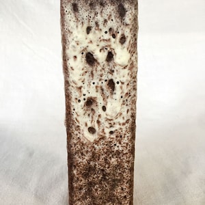 Puede incluir: Un jarrón de cerámica alto y rectangular con un esmalte moteado marrón y blanco. El esmalte tiene un aspecto texturizado y burbujeante.