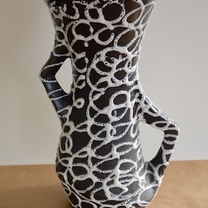 May include: A black and white ceramic vase with a red rim and a unique, abstract design. The vase has two handles and a wide opening.