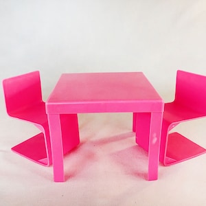 Puede incluir: Un juego de mesa y dos sillas de plástico rosa. La mesa y las sillas son todas del mismo color rosa brillante.