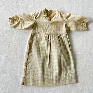 May include: A beige and white gingham dress with a simple, gathered neckline. The dress has long sleeves and a loose, flowing fit.