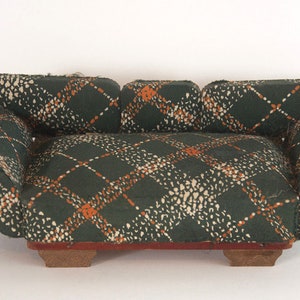 May include: A green, orange, and white patterned fabric sofa with wooden legs. The sofa is a miniature version of a traditional sofa.