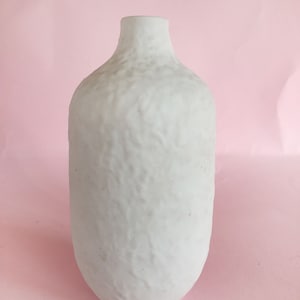 May include: White ceramic vase with a textured surface. The vase has a rounded body and a narrow neck.