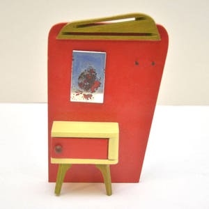Op de afbeelding: Een miniatuur houten poppenhuis meubelset in rood en geel met een klein dressoir en een wandkast met een foto.