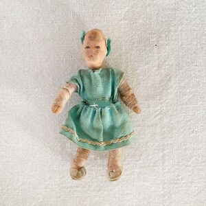 May include: A vintage cloth doll with a light brown face, blue eyes, and a teal dress with a lace trim. The doll has a simple, handmade appearance.