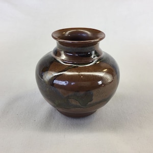 May include: A small, brown ceramic vase with a white and green glaze. The vase has a rounded body and a slightly flared lip.