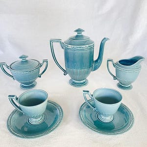 Puede incluir: Juego de té de cerámica azul vintage, que incluye una tetera, azucarero, lechera y dos tazas con platillos. El juego presenta un diseño acanalado con adornos decorativos.