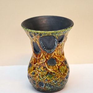 May include: A ceramic vase with a textured, abstract design in shades of yellow, green, and black. The vase has a wide mouth and a narrow base.