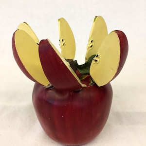 Może przedstawiać: Czerwone jabłko z żółtymi plastrami ułożonymi wokół górnej części, tworząc kształt kwiatu. Jabłko jest przedmiotem dekoracyjnym.