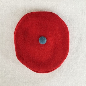 Könnte beinhalten: Eine rote Baskenmütze mit einem blauen Filzknopf oben.