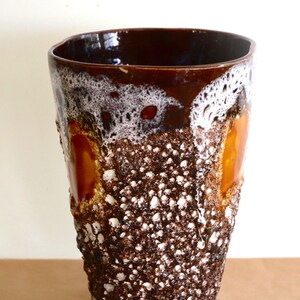 May include: A brown ceramic vase with a textured, speckled surface. The vase has a white and orange glaze with a drip effect.