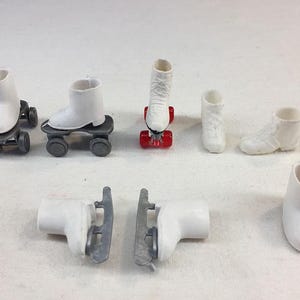 May include: A collection of miniature white roller skates and ice skates. The roller skates have black wheels and gray platforms, while the ice skates have silver blades. The image also includes a pair of white boots.