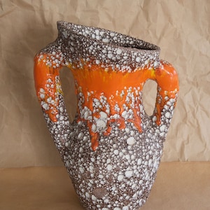May include: A brown and white ceramic vase with orange glaze and two handles. The vase has a textured surface with small white dots.