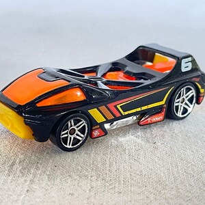 May include: Black and orange toy race car with silver wheels. The car has a number 6 on the side and yellow and red accents. The front of the car is yellow.