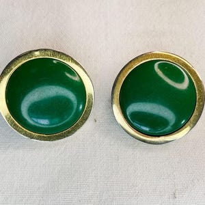 May include: A pair of green and gold earrings. The earrings are round and have a smooth, shiny finish.