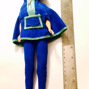 May include: A blue corduroy doll outfit with a green trim and a hooded jacket. The doll is wearing a blue corduroy pantsuit with a green trim and a hooded jacket. The doll is approximately 30 cm tall.
