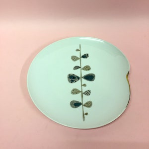 Può includere: Un piatto in ceramica bianca con un bordo dorato e un design floreale stilizzato in tonalità di blu e marrone.