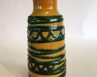 Puede incluir: Un jarrón de cerámica amarillo con patrones geométricos verdes. El jarrón tiene un cuello estrecho y una base ancha.