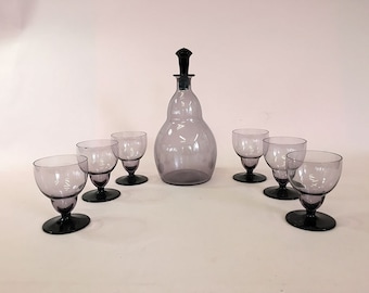 May include: A set of six clear glass decanter and glasses with a purple tint. The decanter has a black stopper.