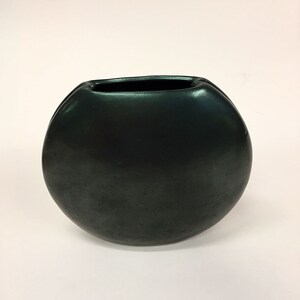 May include: A dark green ceramic vase with a rounded, slightly oval shape. The vase has a wide opening and a smooth, glossy finish.