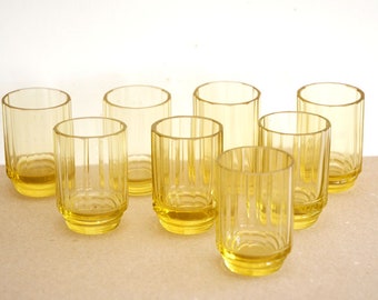 May include: Eight yellow glass tumblers with a ribbed design. The glasses are arranged in two rows of four.