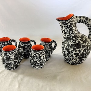 May include: Set of five black and white ceramic mugs with orange rims and a matching black and white ceramic pitcher with an orange rim.