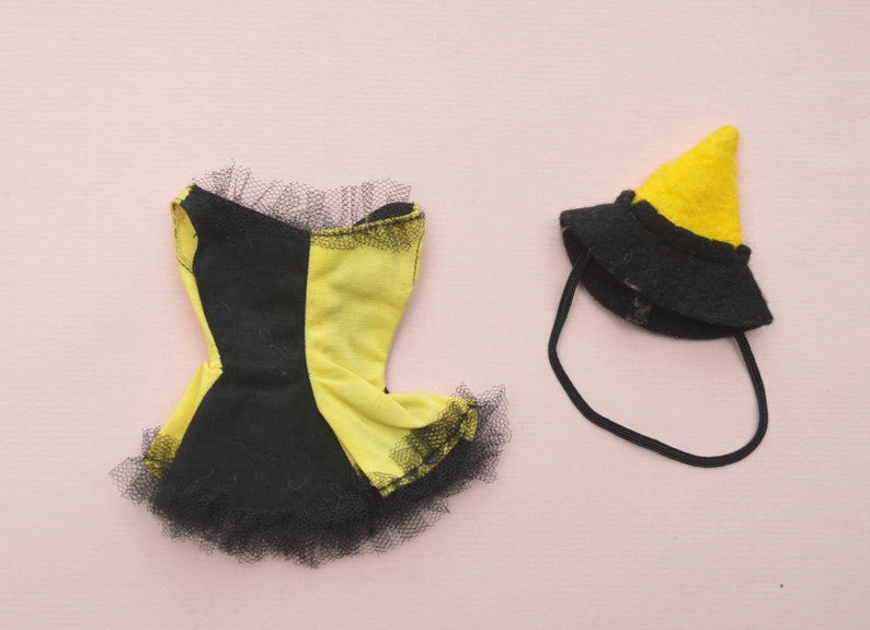 May include: A black and yellow doll dress with a black tulle skirt and a matching black witch hat with a yellow pointed top.