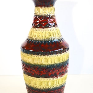 Puede incluir: Un jarrón de cerámica con un patrón geométrico en tonos rojos, amarillos y marrones. El jarrón tiene una base ancha y un cuello estrecho.