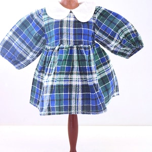 Könnte beinhalten: Ein blaues und grünes kariertes Kleid mit weißem Kragen. Das Kleid hat lange Ärmel und einen gerafften Rock. Es wird auf einer Holzpuppe präsentiert.