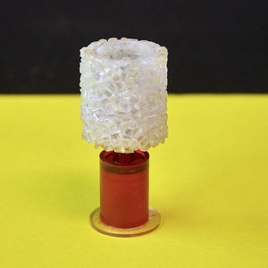 May include: A miniature table lamp with a white, textured lampshade and a red base.