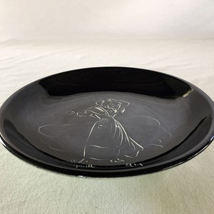Könnte beinhalten: Ein schwarzer Keramikteller mit einer weißen Silhouette einer Frau in einem Kleid. Der Teller hat einen leicht erhöhten Rand.