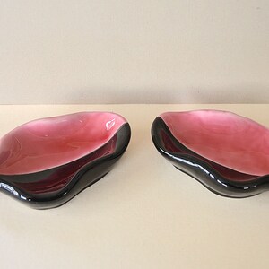 May include: Two small, black and pink ceramic dishes. The dishes are shaped like a leaf and have a glossy finish.