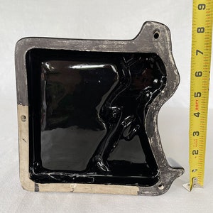 K&ouml;nnte beinhalten: Schwarze Keramikform mit einem erhabenen Design einer Person. Die Form ist rechteckig und hat eine glatte, gl&auml;nzende Oberfl&auml;che.