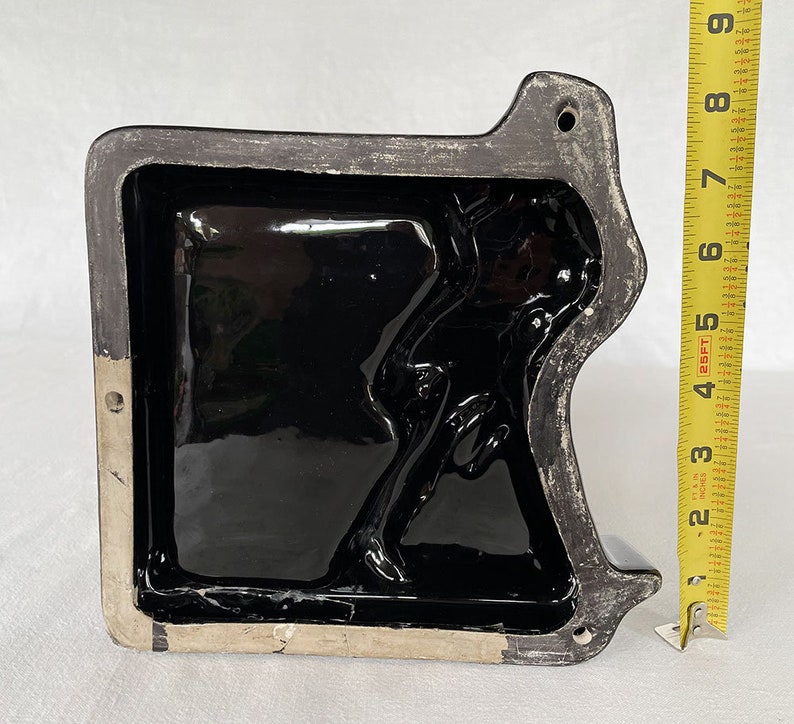 K&ouml;nnte beinhalten: Schwarze Keramikform mit einem erhabenen Design einer Person. Die Form ist rechteckig und hat eine glatte, gl&auml;nzende Oberfl&auml;che.