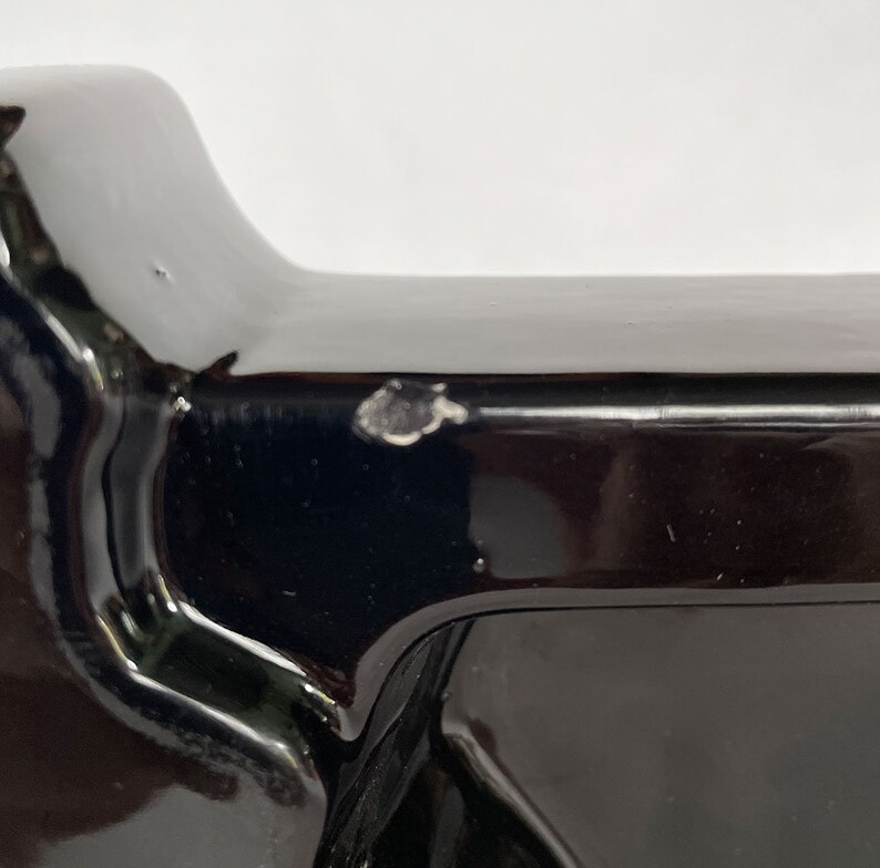 K&ouml;nnte beinhalten: Ein schwarzes Keramikobjekt mit einer glatten, gl&auml;nzenden Oberfl&auml;che. Das Objekt hat eine rechteckige Form mit abgerundeten Kanten und einer leichten W&ouml;lbung an der Oberseite. Auf der Oberfl&auml;che befindet sich eine kleine wei&szlig;e Markierung.