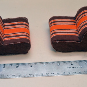 May include: Two miniature brown fabric armchairs with orange and white striped upholstery. The armchairs are approximately 7.5 cm long.