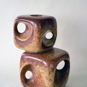 May include: Two stacked ceramic candle holders with a brown and yellow glaze. Each holder has a square shape with three circular cutouts.